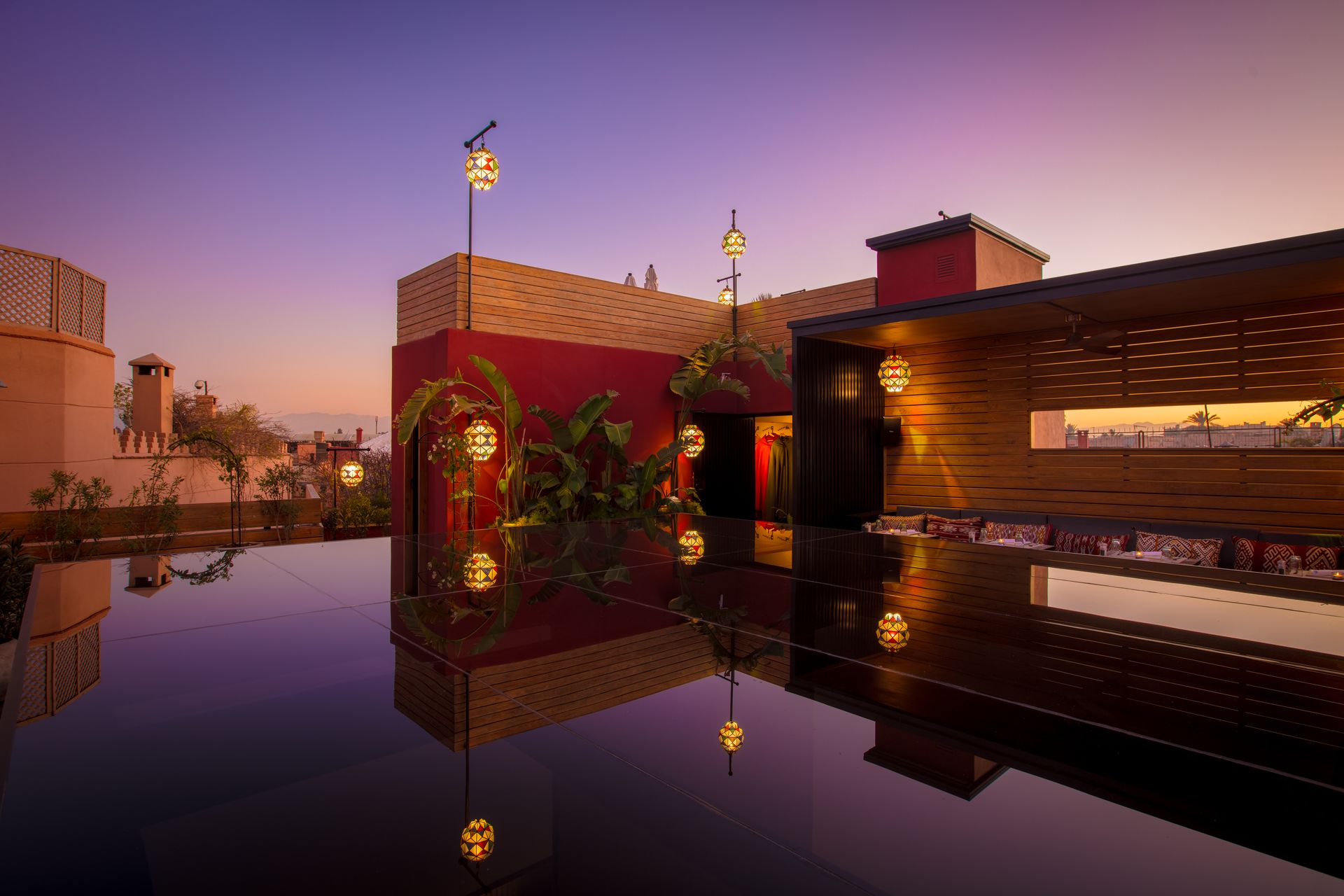 The rooftop terrace at dusk — lanterns glowing above mirror-black tables under a violet sky